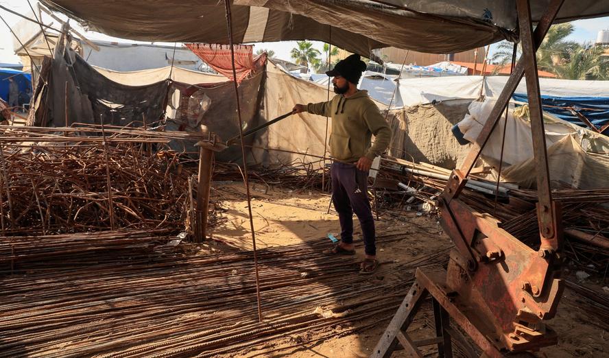 A Palestinian worker reshapes and straightens steel bars recovered from destroyed homes using basic tools inside a small workshop in Khan Younis, southern Gaza Strip, December 10, 2025