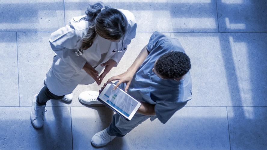 A bird's eye view of two medical professionals reviewing a chart in a hospital corridor. Photo by Hispanolistic/Getty Images