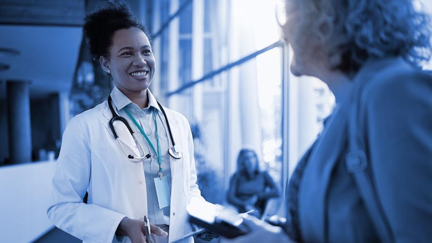 A smiling medical professional cheerfully speaks with an older female patient. Photo by Drazen Zigic/Getty Images