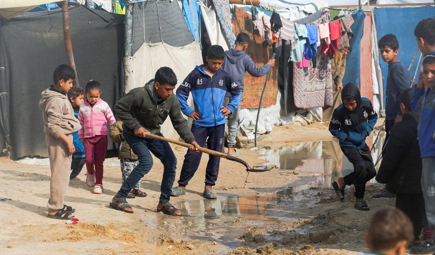Displaced Palestinian children clear a waterlogged area near tents at a camp in Khan Younis in the southern Gaza Strip, February 24, 2026